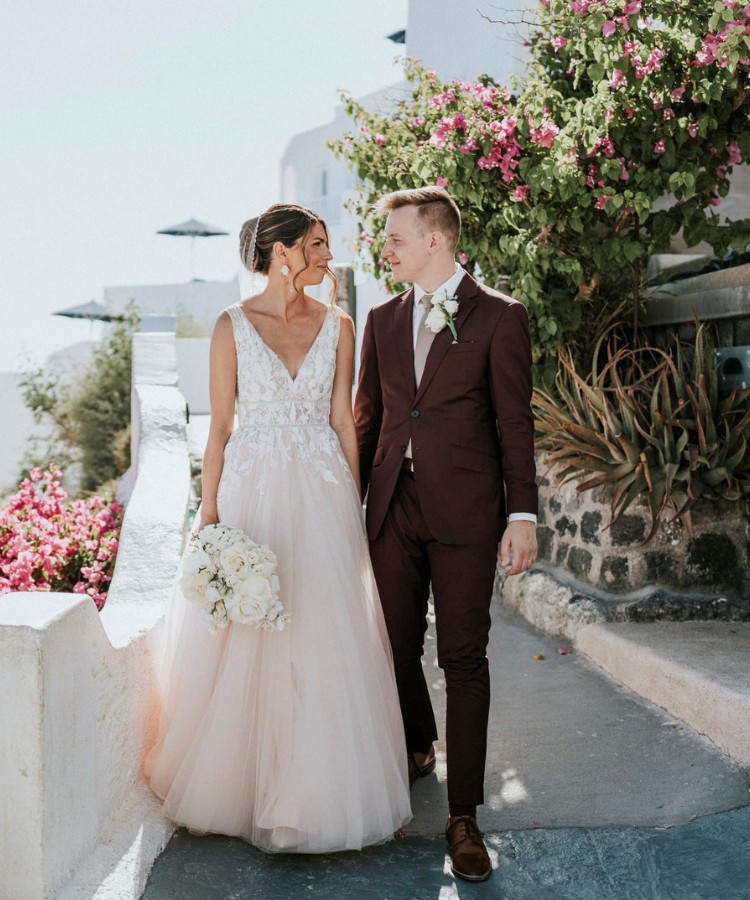 Bride and groom walking together in a sunny outdoor setting, with the groom wearing a custom burgundy suit and the bride in a white wedding dress.