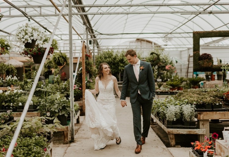 Bride and groom walking through a greenhouse, with the groom wearing a custom dark green suit and the bride in a white lace wedding dress.