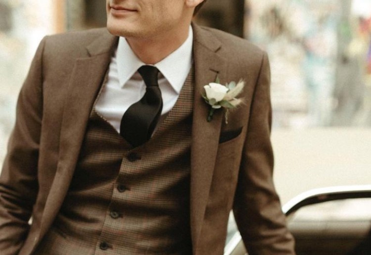 Groom wearing a custom brown three-piece suit by Eph Apparel with a boutonniere.