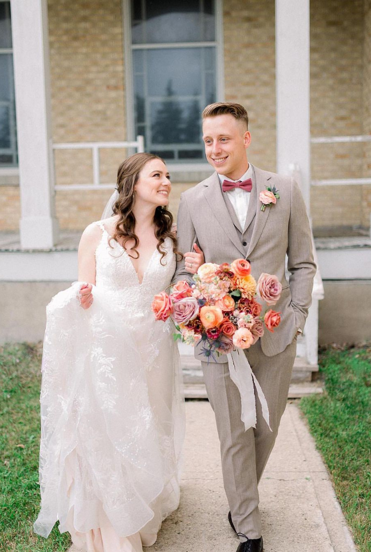 Bride and groom walking arm-in-arm, with the groom in a beige suit and the bride holding a colorful bouquet