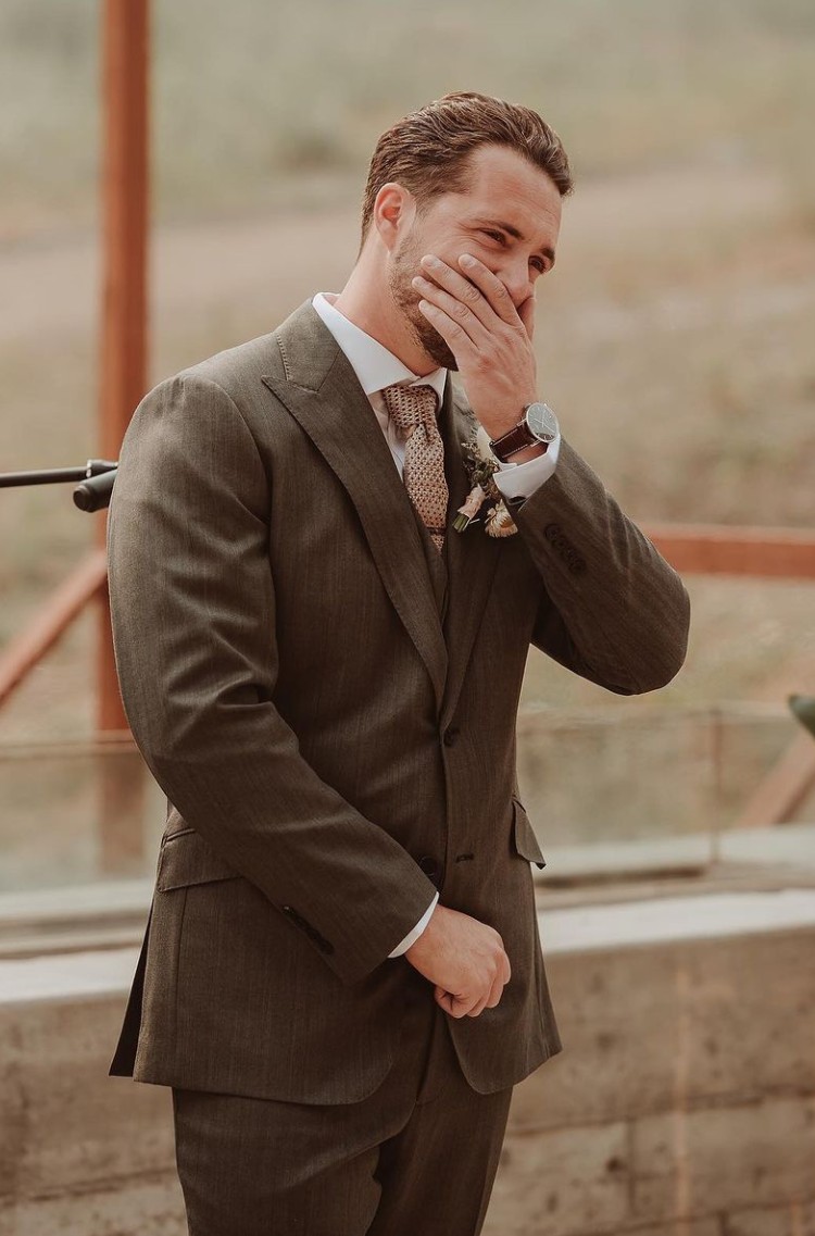 Groom in a brown suit from Eph Apparel, holding back tears at his wedding ceremony.