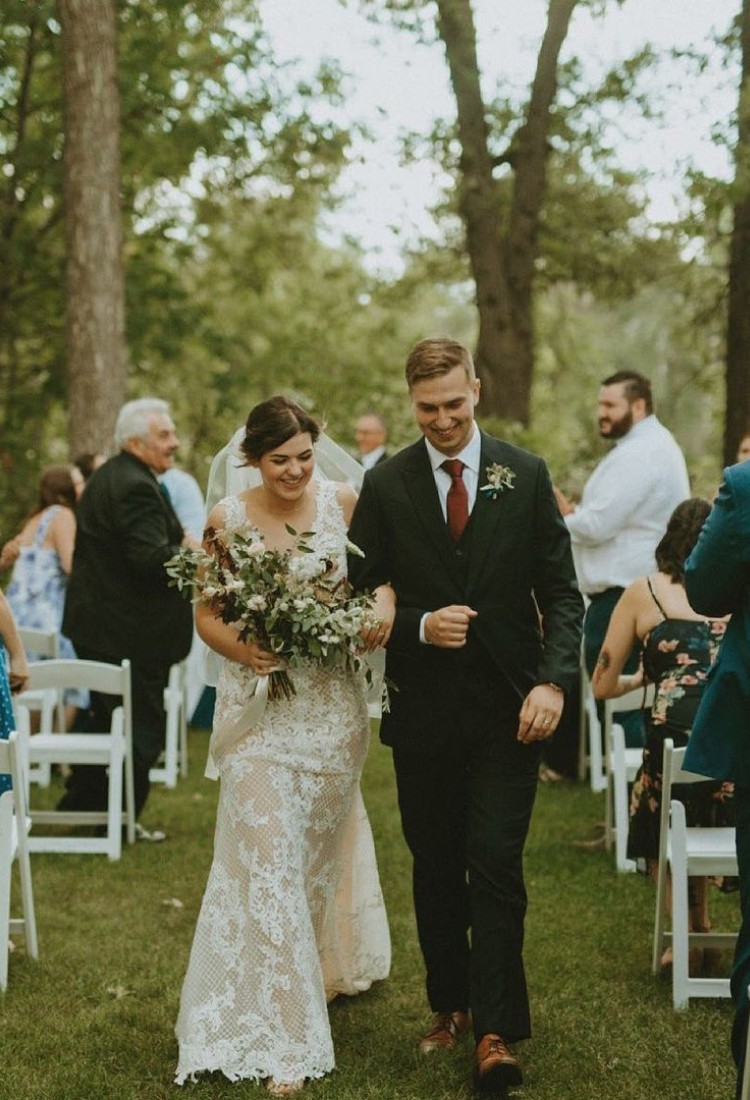 Bride and groom walking down the aisle at an outdoor wedding, with the groom wearing a custom green suit from Eph Apparel.