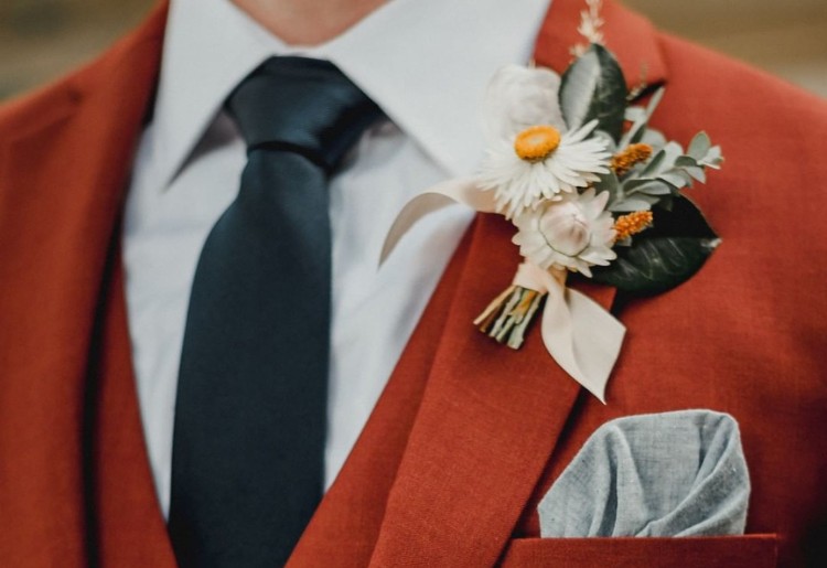 Close-up of a groom wearing an orange suit with a black tie, featuring a floral boutonniere and a pocket square.