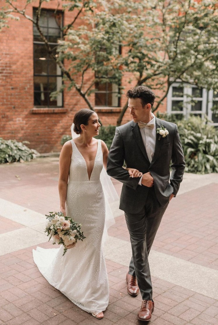 Bride and groom walking arm in arm, with the groom wearing a custom grey suit and the bride in a sleeveless wedding gown.