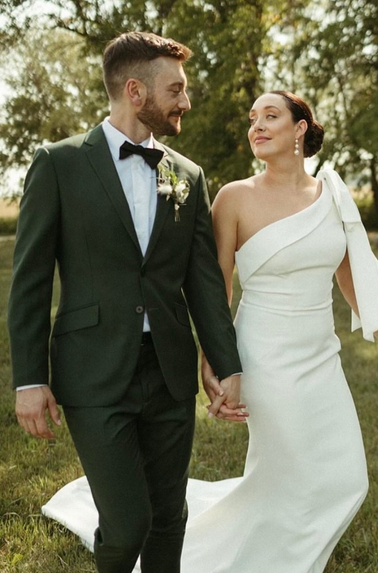 Groom in a custom green suit holding hands with the bride in an elegant white gown.